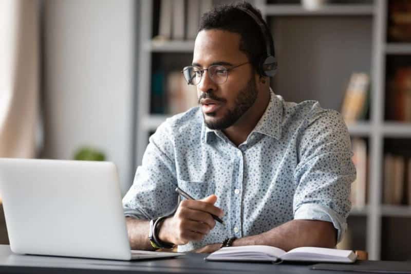 Estudante do MBA de UX Design assistindo a aula no laptop e anotando informações - MBA UX Design